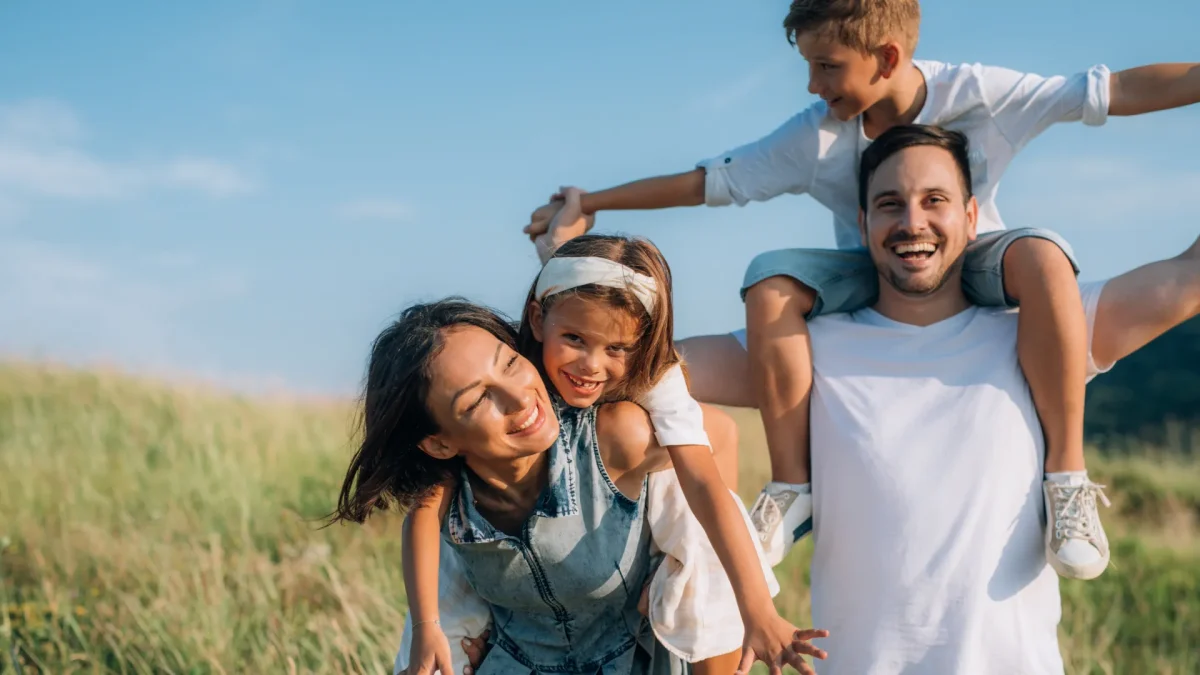 Glückliche Familie spielt im Freien, Symbol für eine liebevolle Kinder- & Jugendhilfeeinrichtung, bei sonnigem Wetter und grüner Natur, Lächeln und Freude auf allen Gesichtern.