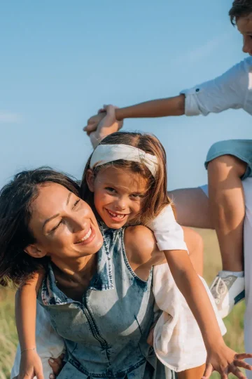 Glückliche Familie spielt im Freien, Symbol für eine liebevolle Kinder- & Jugendhilfeeinrichtung, bei sonnigem Wetter und grüner Natur, Lächeln und Freude auf allen Gesichtern.
