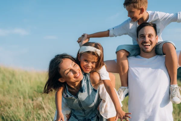 Glückliche Familie spielt im Freien, Symbol für eine liebevolle Kinder- & Jugendhilfeeinrichtung, bei sonnigem Wetter und grüner Natur, Lächeln und Freude auf allen Gesichtern.