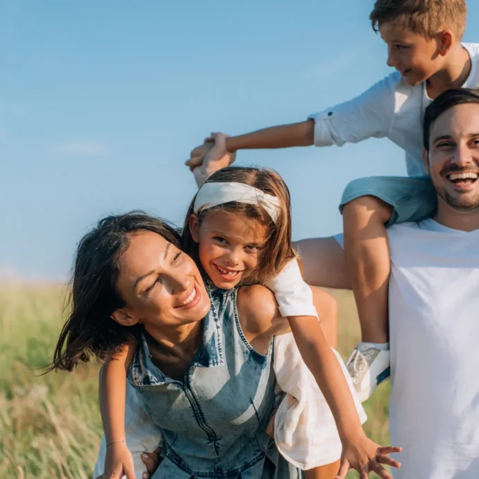 Glückliche Familie spielt im Freien, Symbol für eine liebevolle Kinder- & Jugendhilfeeinrichtung, bei sonnigem Wetter und grüner Natur, Lächeln und Freude auf allen Gesichtern.