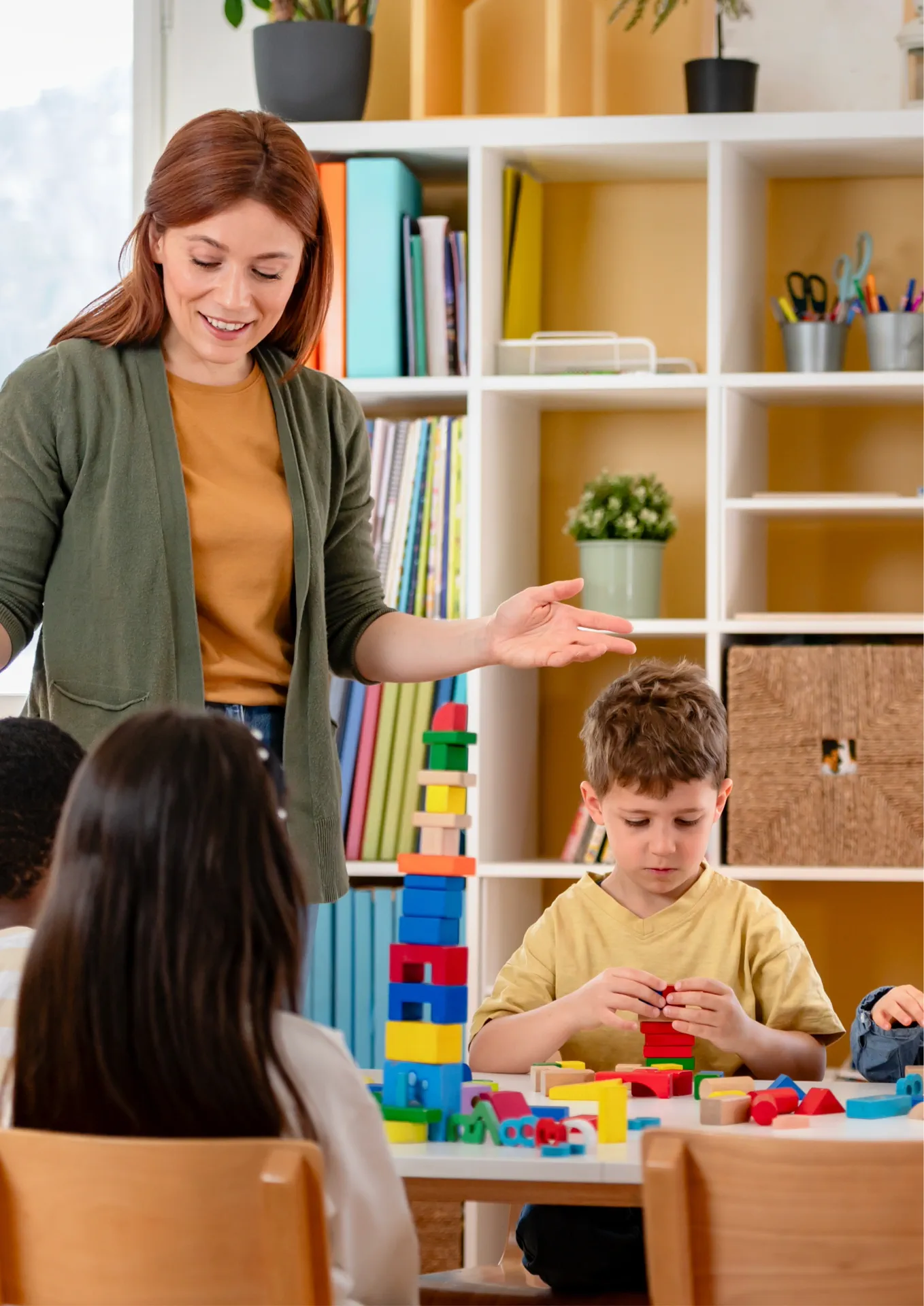 Erzieherin spielt mit Kindern in einer freundlichen Kinder- & Jugendhilfeeinrichtung, Kinder bauen zusammen bunte Türme mit Bauklötzen, fördernde Lernumgebung.