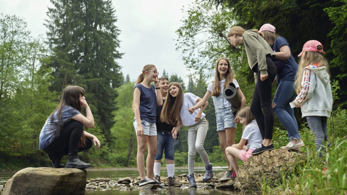 Gruppe fröhlicher Kinder und Jugendlicher bei einem Ausflug in der Natur, organisiert von einer modernen Kinder- & Jugendhilfeeinrichtung, fördert Gemeinschaft und Abenteuerlust.