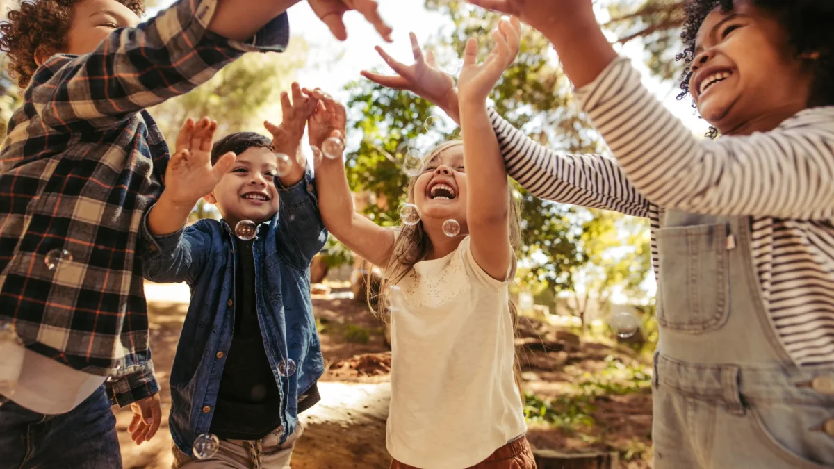 Kinder spielen lachend im Freien und fangen Seifenblasen in einer freundlichen Kinder- & Jugendhilfeeinrichtung.