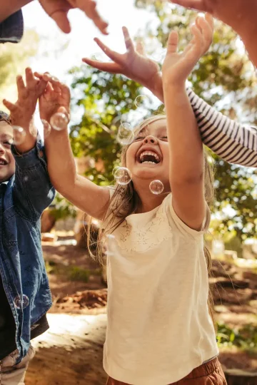 Kinder spielen lachend im Freien und fangen Seifenblasen in einer freundlichen Kinder- & Jugendhilfeeinrichtung.