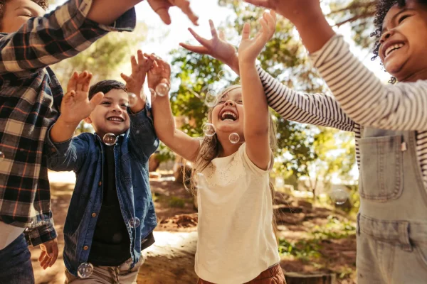 Kinder spielen lachend im Freien und fangen Seifenblasen in einer freundlichen Kinder- & Jugendhilfeeinrichtung.