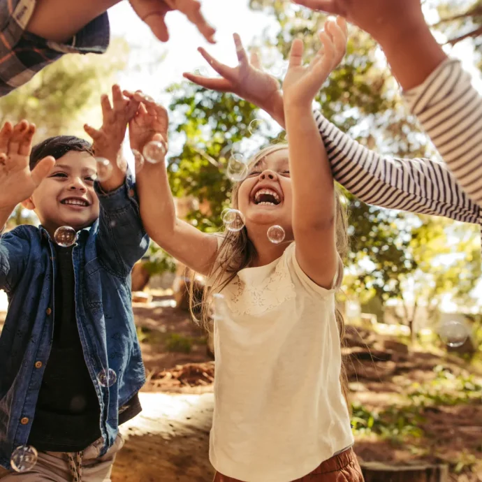 Kinder spielen lachend im Freien und fangen Seifenblasen in einer freundlichen Kinder- & Jugendhilfeeinrichtung.