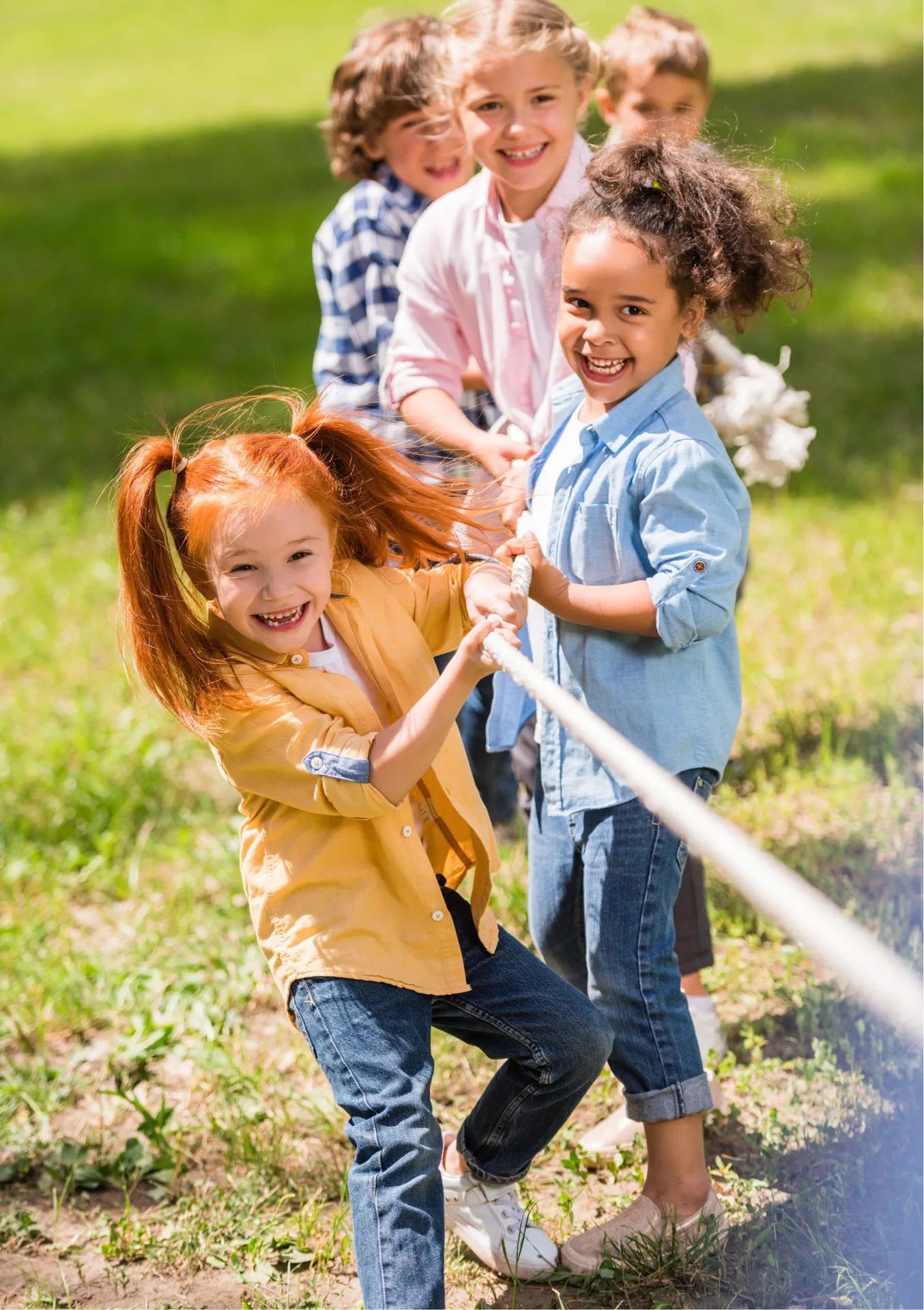 Glückliche Kinder spielen Tauziehen im Freien, symbolisieren Teamgeist und Freude in einer modernen Kinder- & Jugendhilfeeinrichtung.
