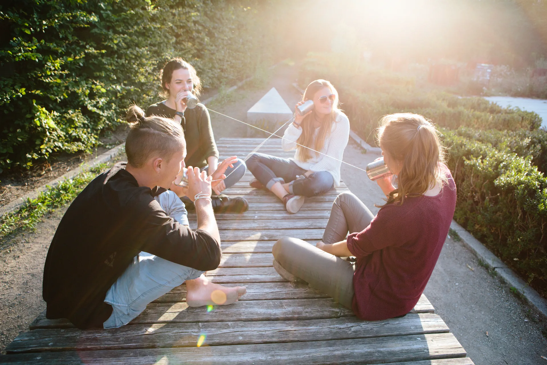 Vier Jugendliche sitzen lachend auf einem Holzsteg in einer sonnigen Umgebung, symbolisieren Gemeinschaft und positive Atmosphäre in einer modernen Kinder- & Jugendhilfeeinrichtung.